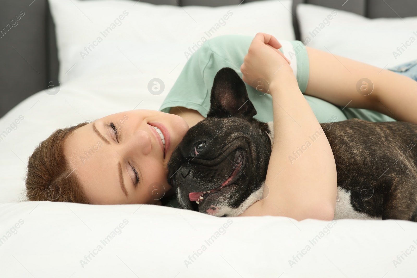 Photo of Happy woman hugging cute French Bulldog on bed in room