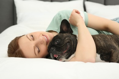 Photo of Happy woman hugging cute French Bulldog on bed in room