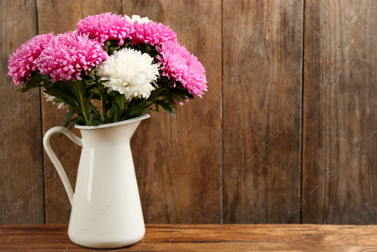 Photo of Beautiful asters in jug on table against wooden background, space for text. Autumn flowers