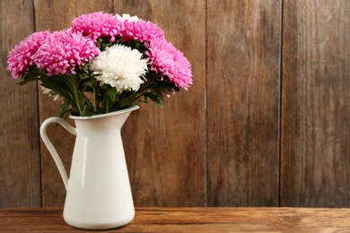 Beautiful asters in jug on table against wooden background, space for text. Autumn flowers