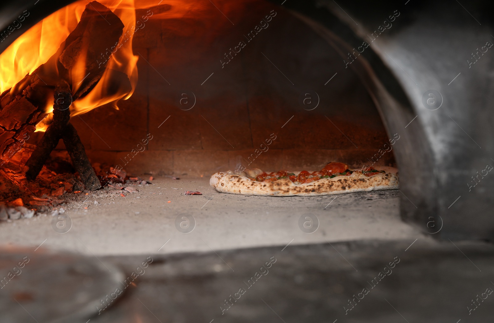 Photo of Burning firewood and tasty pizza in oven at restaurant kitchen