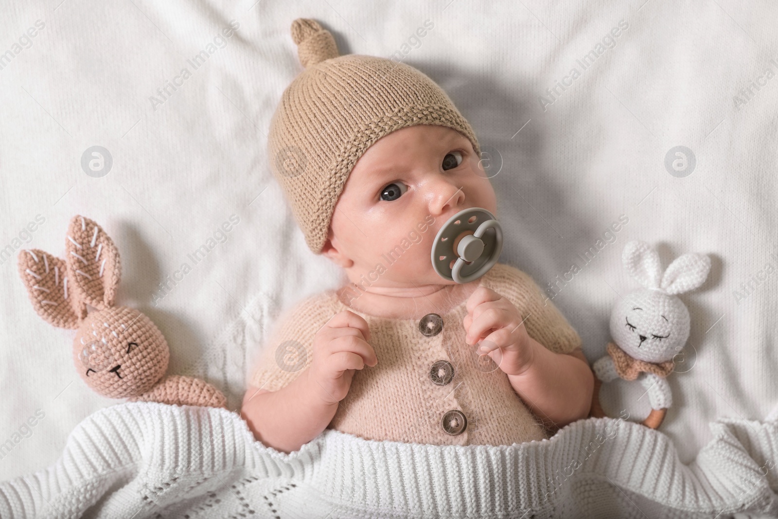Photo of Cute newborn baby with pacifier and toys on white knitted plaid, top view