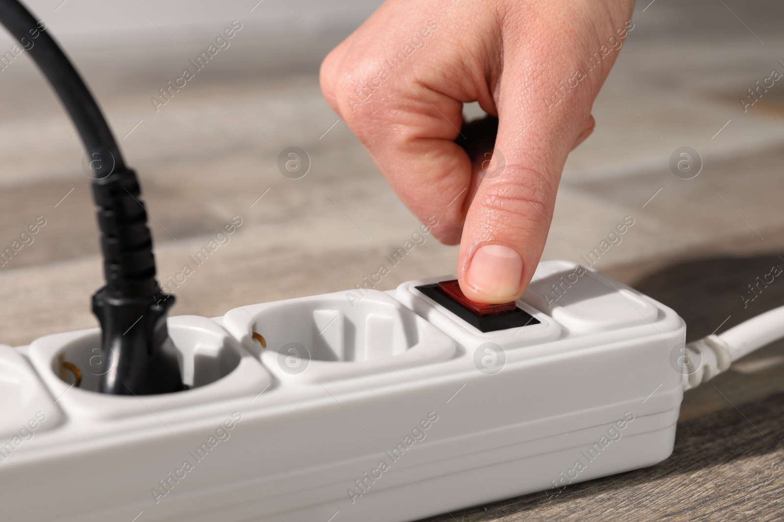 Photo of Man pressing power button of extension board on floor, closeup