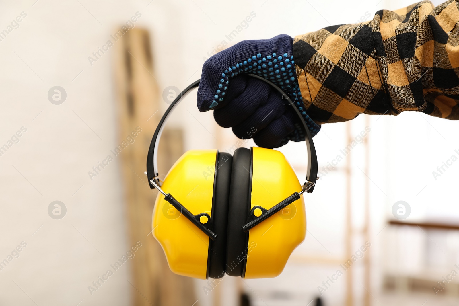 Photo of Worker holding safety headphones indoors, closeup. Hearing protection device