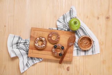 Photo of Slices of fresh apple with nut butter, blueberries and peanuts on wooden table, flat lay