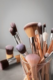 Photo of Set of professional makeup brushes on grey table, closeup