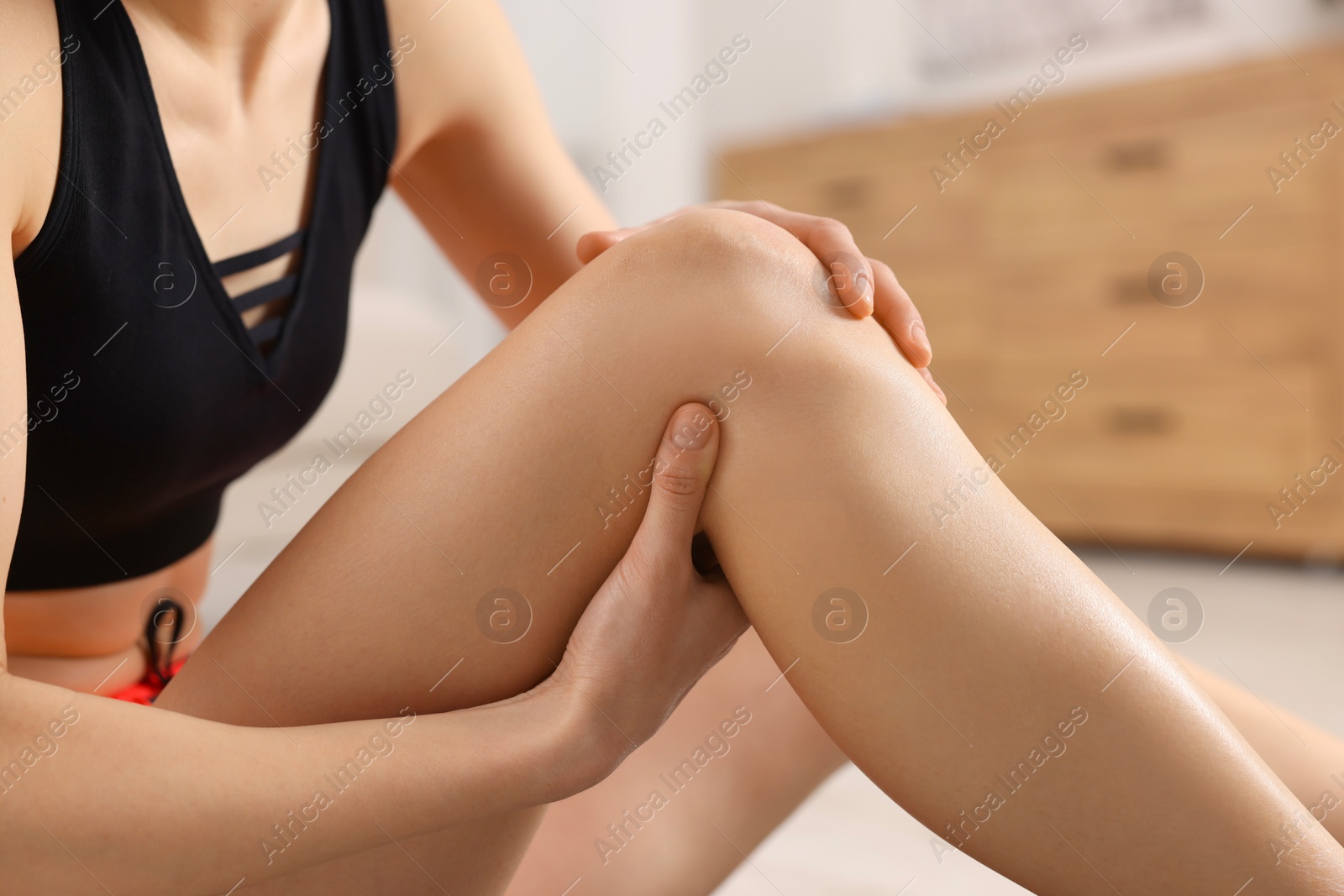 Photo of Woman suffering from leg pain in room, closeup