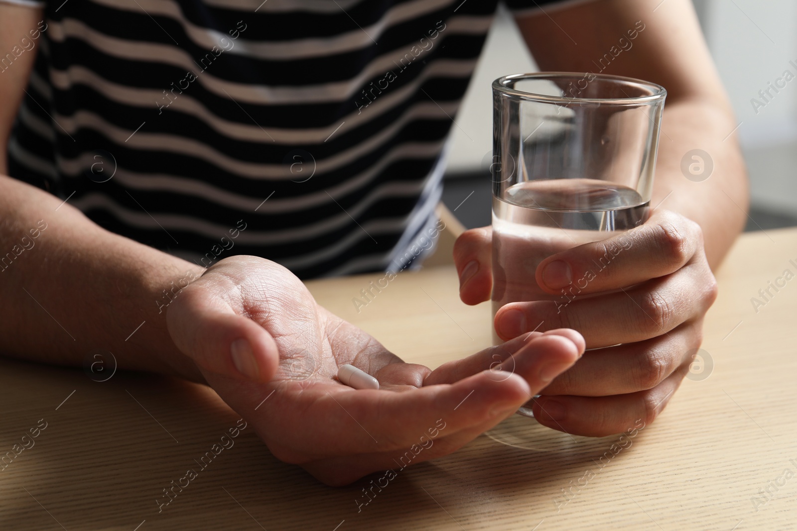 Photo of Man with glass of water and pill at wooden table, closeup