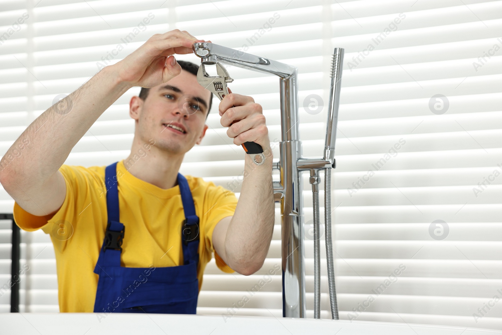 Photo of Smiling plumber repairing faucet with spanner in bathroom