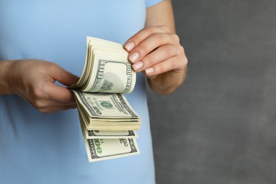 Money exchange. Woman counting dollar banknotes on grey background, closeup. Space for text