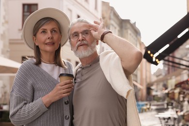 Affectionate senior couple with coffee walking outdoors, space for text