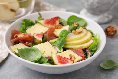 Photo of Tasty salad with brie cheese, prosciutto, pear and figs on grey table, closeup