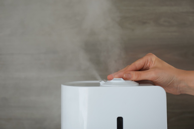 Photo of Woman using modern air humidifier against wooden background, closeup