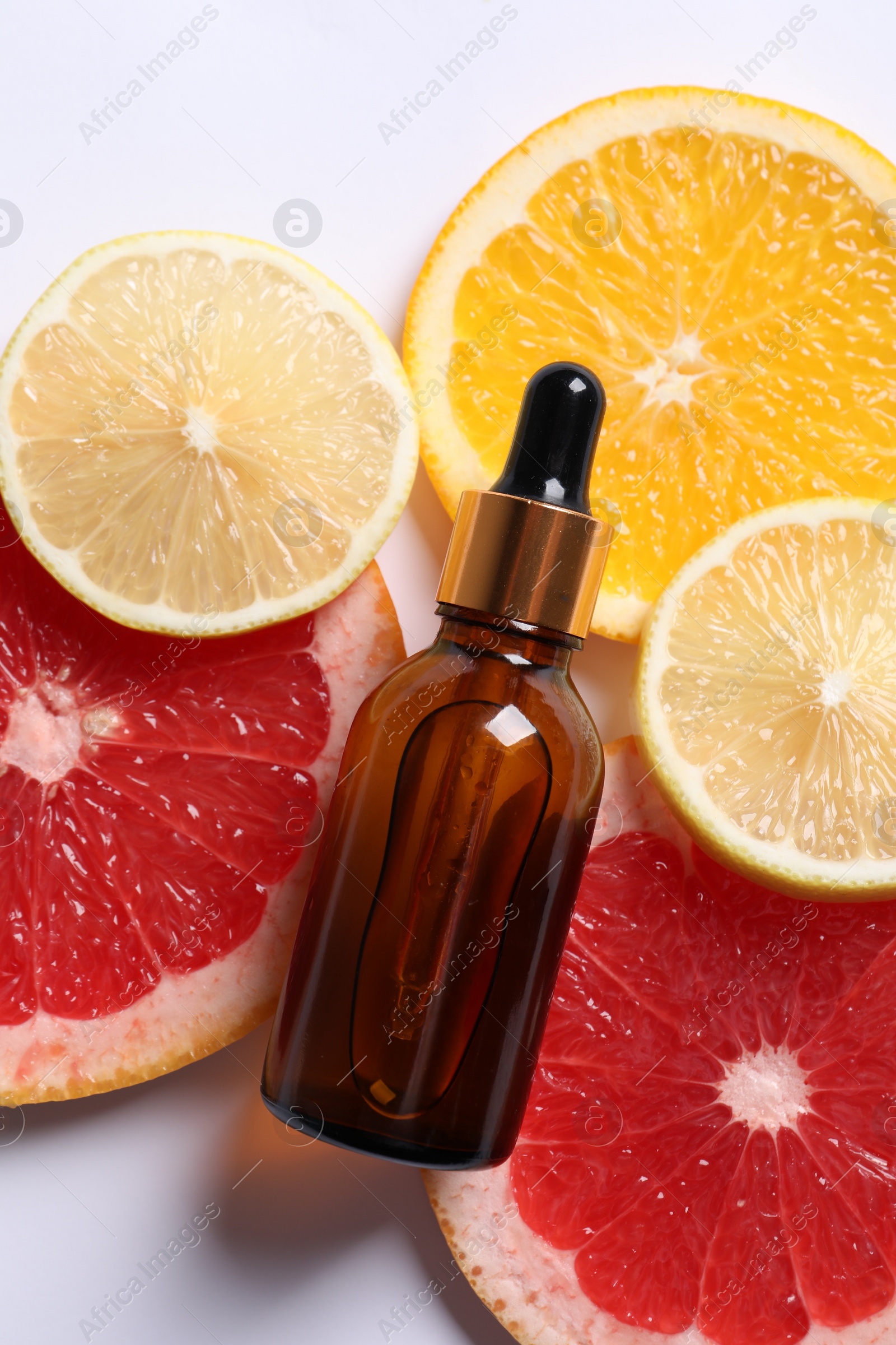 Photo of Bottle of cosmetic serum and sliced citrus fruits on white background, flat lay