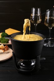 Dipping piece of ham into fondue pot with melted cheese on table