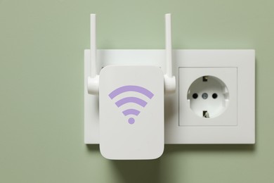 Image of New modern repeater with Wi-Fi symbol plugged into socket on light green wall