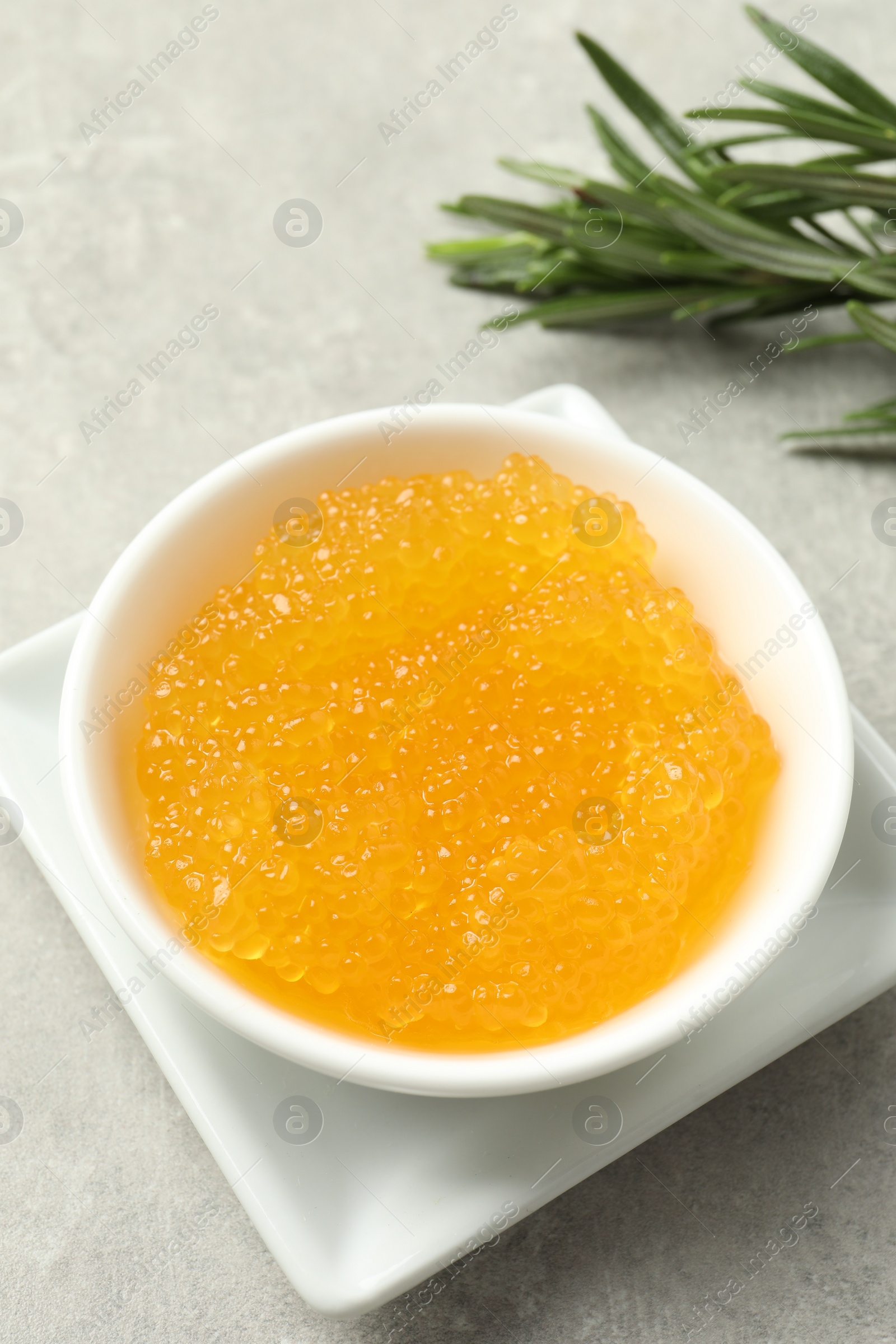 Photo of Fresh pike caviar in bowl and rosemary on light grey table, closeup