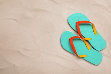 Pair of turquoise flip flops on sand, flat lay. Space for text