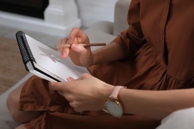 Photo of Woman drawing in sketchbook with pencil at home, closeup