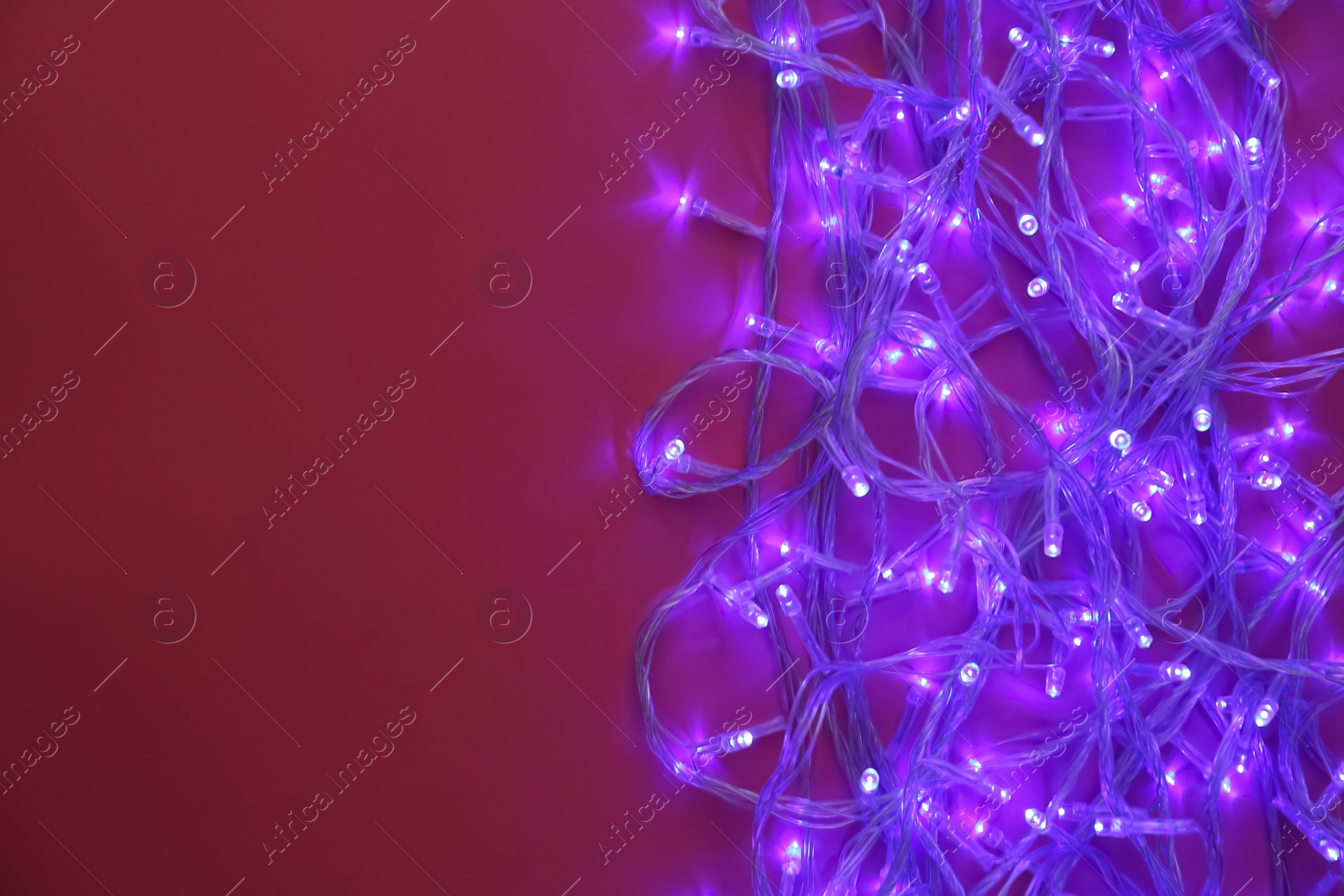 Photo of Glowing Christmas lights on burgundy background, top view. Space for text