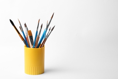 Photo of Holder with different paint brushes on white background. Space for text