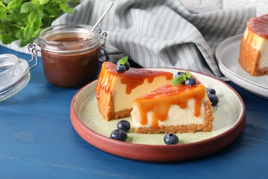Pieces of delicious caramel cheesecake with blueberry and mint on blue wooden table
