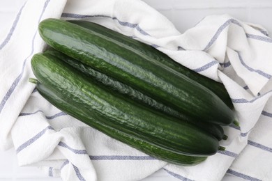 Photo of Fresh cucumbers and cloth on white table, top view