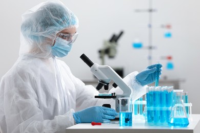 Scientist taking test tube while working with microscope in laboratory