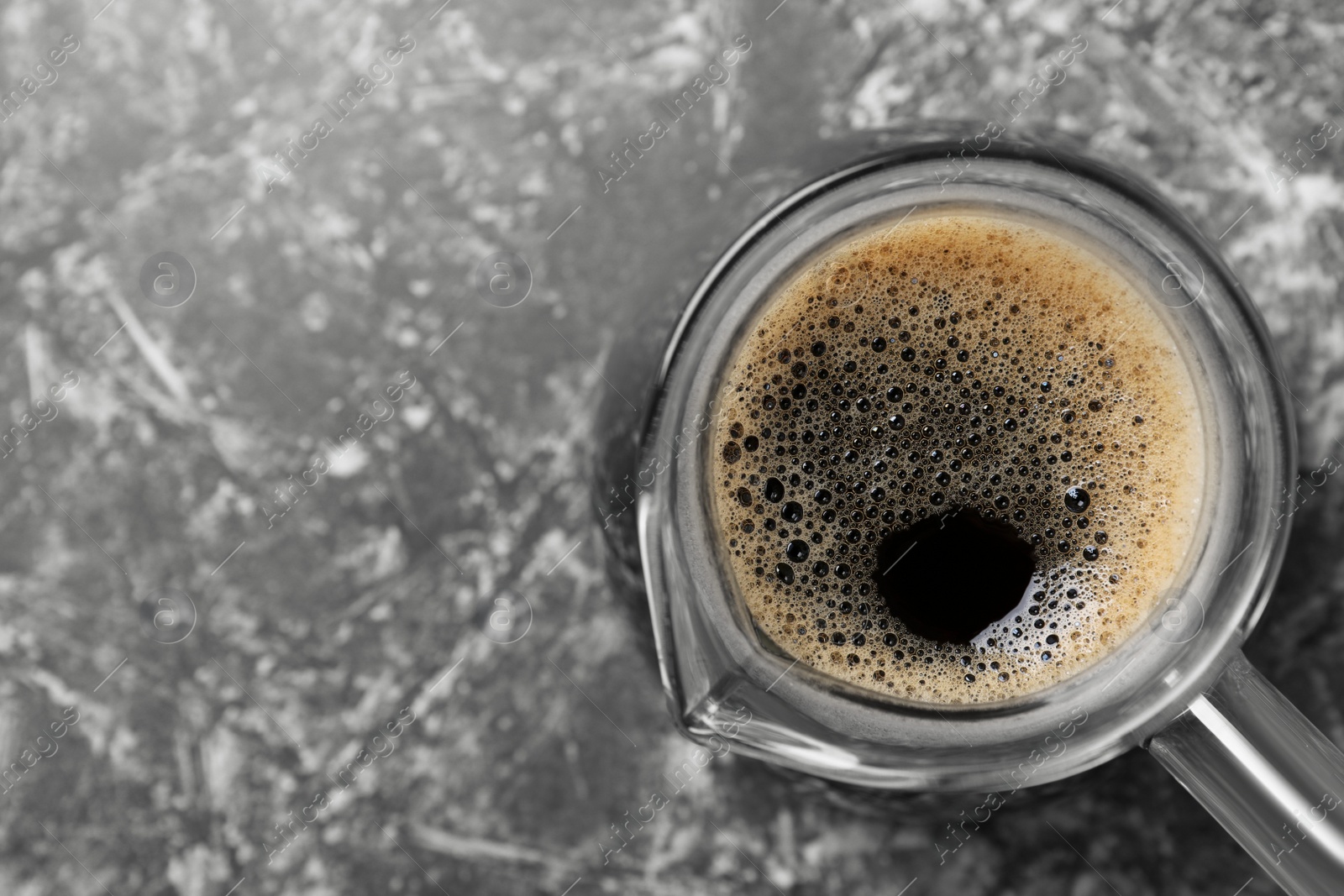 Photo of Turkish coffee in glass cezve on grey marble table, top view. Space for text