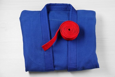 Photo of Red karate belt and blue kimono on wooden background, top view