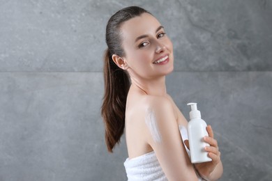 Photo of Happy woman with bottle of body cream near grey wall, space for text