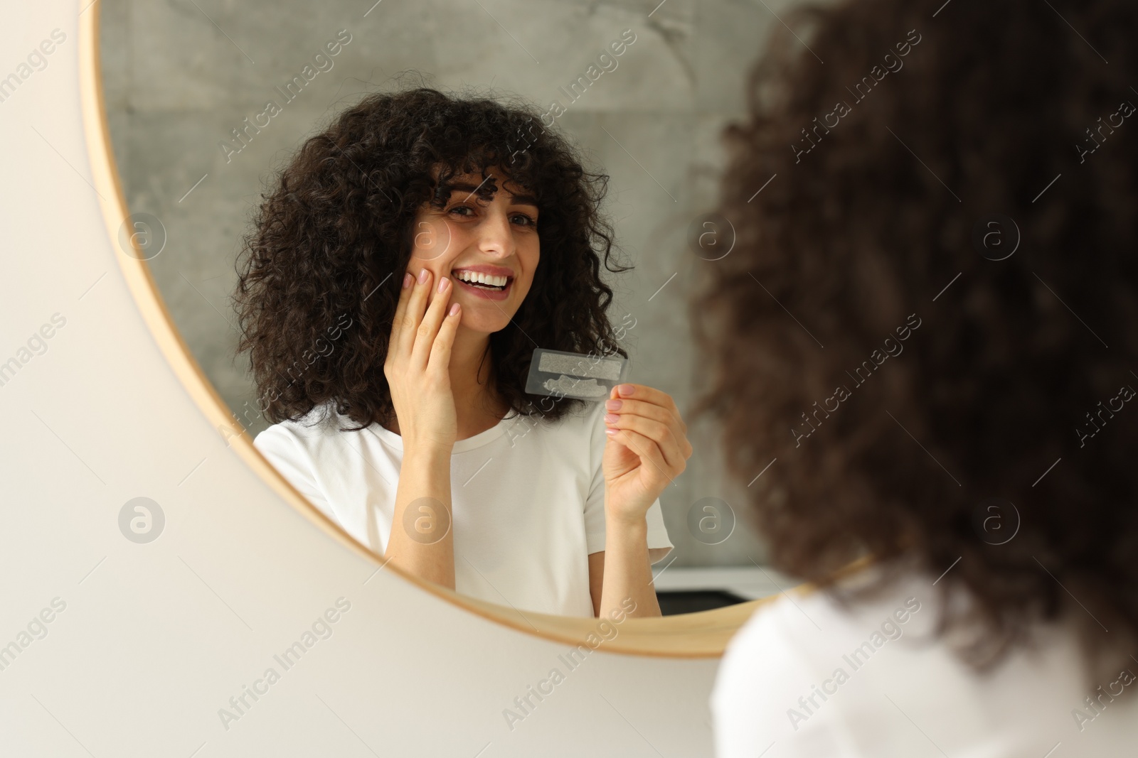 Photo of Young woman holding teeth whitening strips indoors