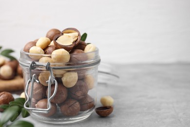 Photo of Tasty Macadamia nuts in jar on light grey table, closeup. Space for text