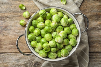 Photo of Colander with Brussels sprouts on wooden background, top view