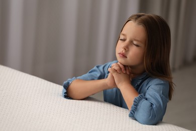 Photo of Cute little girl with hands clasped together saying bedtime prayer in bedroom. Space for text