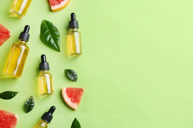 Flat lay composition with bottles of grapefruit essential oil on green background. Space for text