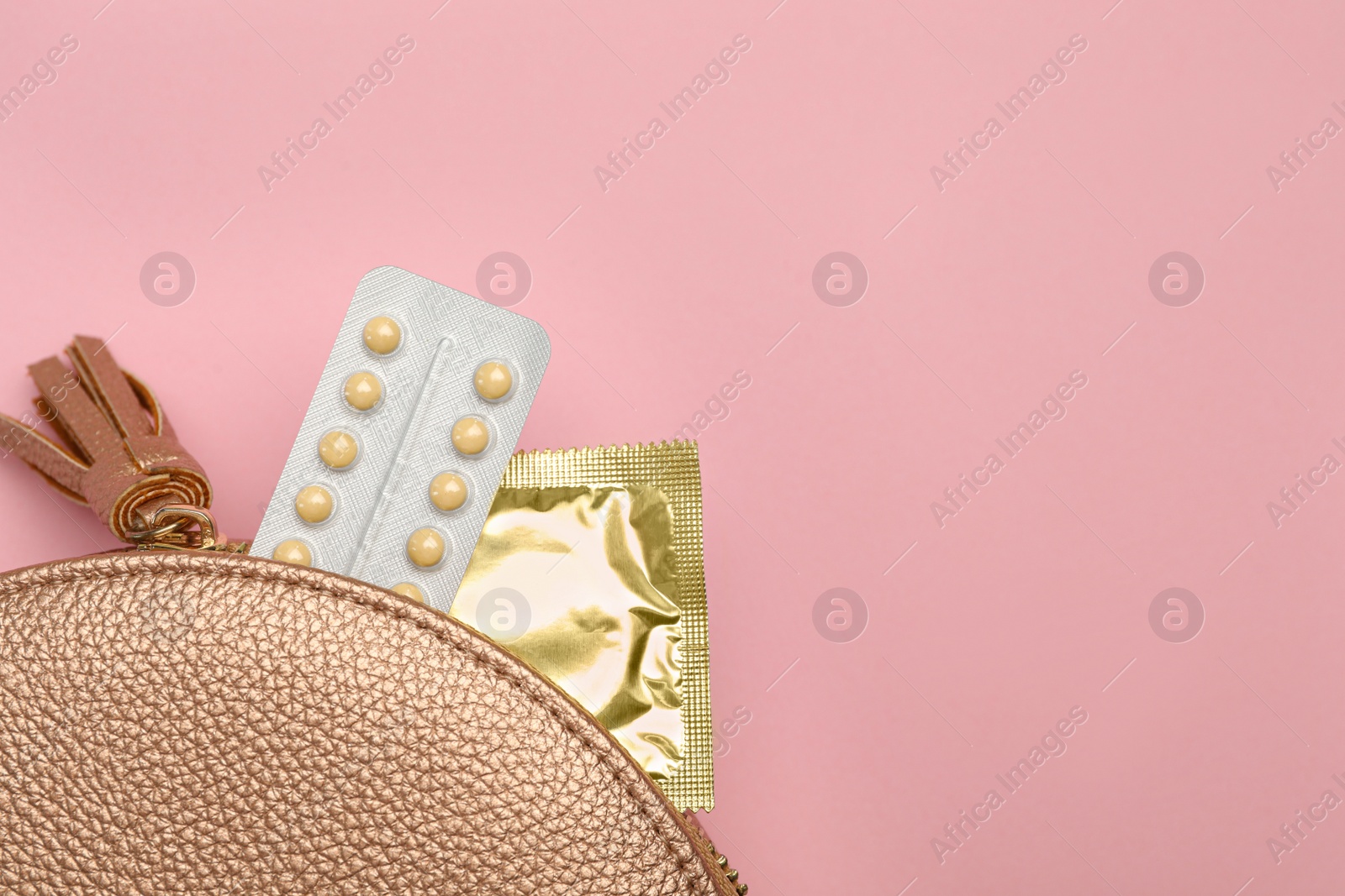 Photo of Condom and birth control pills in purse on pink background, top view with space for text. Safe sex