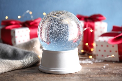 Magical empty snow globe with Christmas presents on wooden table