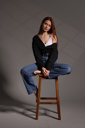 Photo of Beautiful young woman sitting on stool against gray background