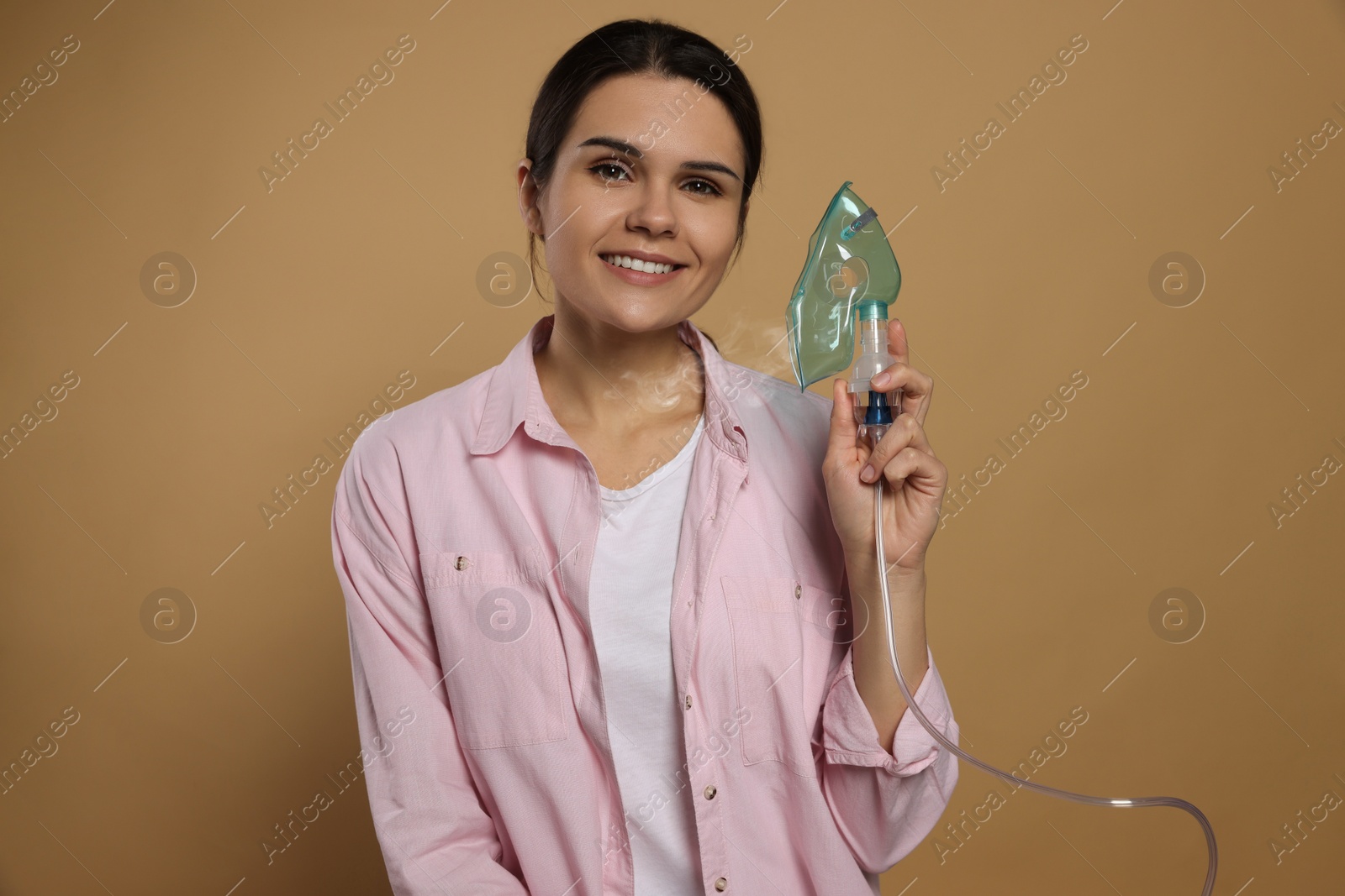 Photo of Happy young woman with nebulizer on dark beige background