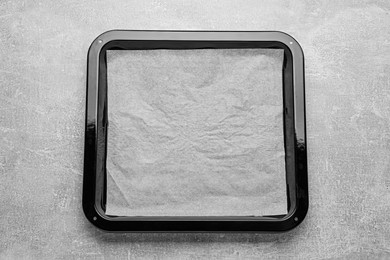 Photo of Baking pan with parchment paper on light grey table, top view. Space for text