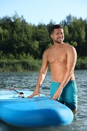 Photo of Man standing near SUP board in river water on sunny day