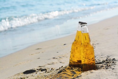 Photo of Bottles of cold beer on sandy beach near sea, space for text