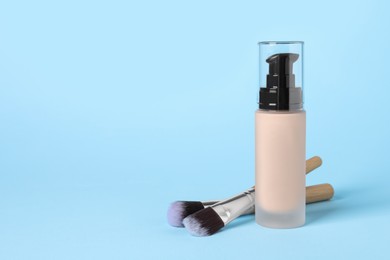 Photo of Bottle of skin foundation and brushes on light blue background, space for text. Makeup product