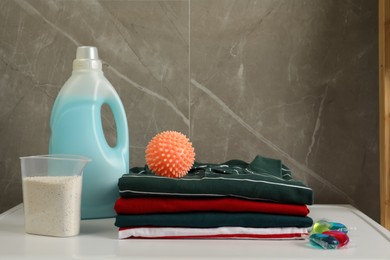 Photo of Orange dryer ball and stacked clean clothes near laundry detergents on white table