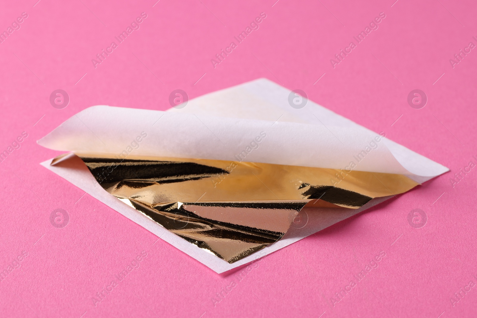 Photo of Edible gold leaf sheet on pink background, closeup