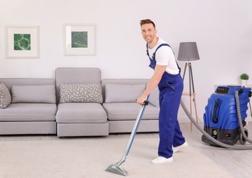 Photo of Male worker removing dirt from carpet with professional vacuum cleaner indoors