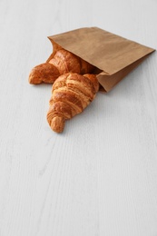 Photo of Paper bag with pastry on light wooden background. Space for text