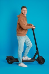 Photo of Happy man with modern electric kick scooter on light blue background