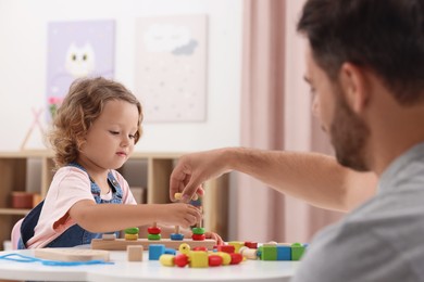 Motor skills development. Father and daughter playing with stacking and counting game at table indoors